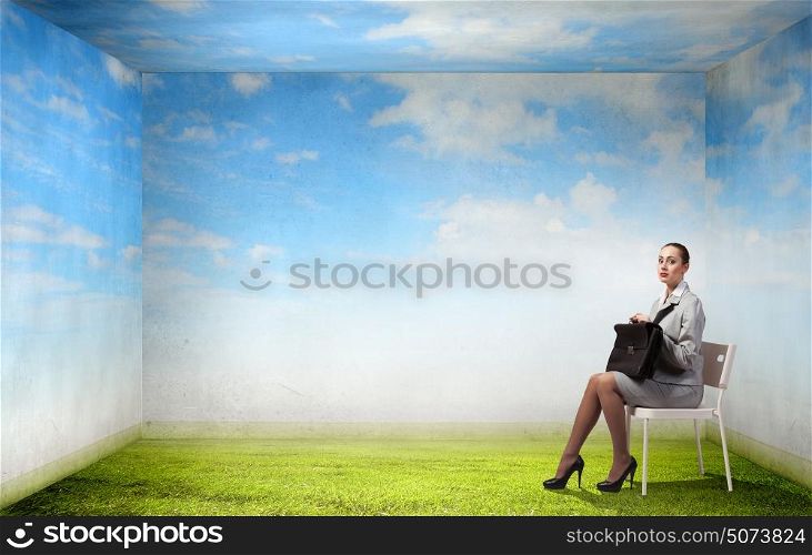 Young pretty businesswoman sitting on chair with briefcase in hands. Taking break from office