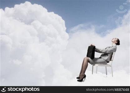 Young pretty businesswoman with briefcase in hands sitting on cloud . Taking break from office