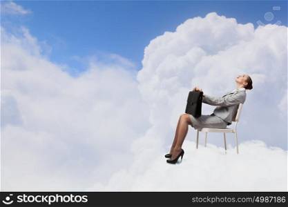 Young pretty businesswoman with briefcase in hands sitting on cloud . Taking break from office