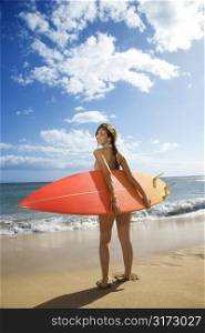 Young pretty Caucasian woman in bikini standing with surfboard at beach in Maui Hawaii.