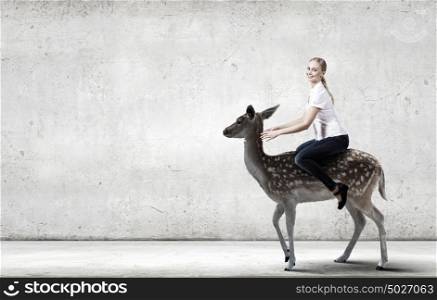 Young pretty fearless woman riding deer animal. Woman ride deer
