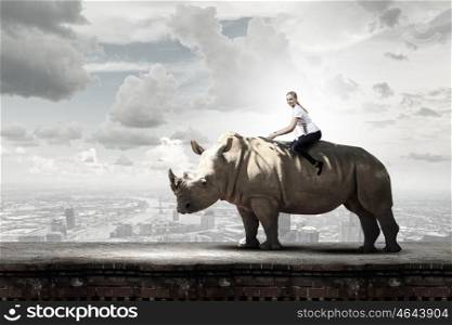 Young pretty fearless woman riding huge rhino. Woman ride rhino