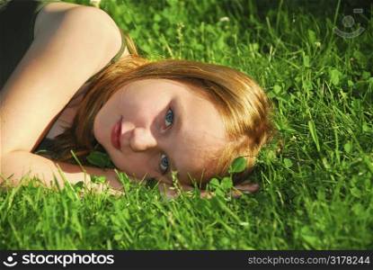 Young pretty girl lying on green grass outside