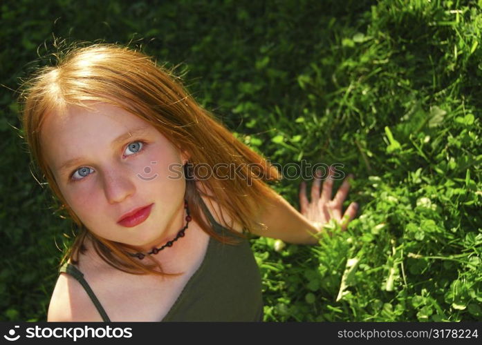 Young pretty girl sitting on green grass outside