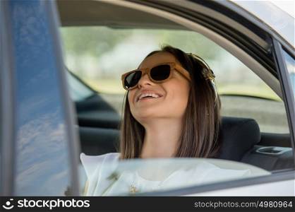 Young pretty girl wearing sunglasses listening music with headphones in car. Summer fun