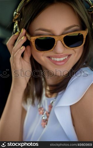 Young pretty girl wearing sunglasses listening music with headphones in car. Summer fun