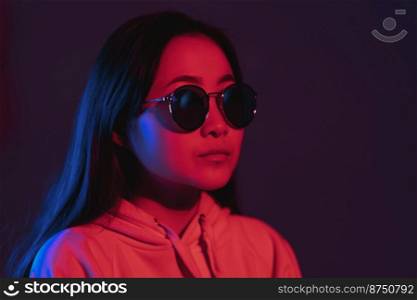 Young pretty girl with asian appearance in neon pink and blue lights at night. Serious trendy hipster teenager in glasses.. Young pretty girl with asian appearance in neon pink and blue lights at night. Serious trendy hipster teenager in glasses