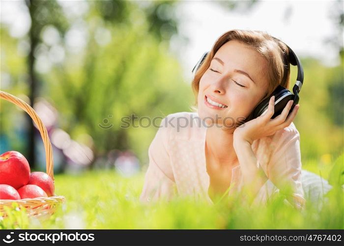 Young pretty lady in park listening to music. Sunny weekend in park