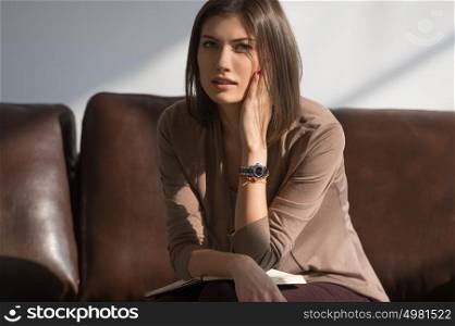 Young pretty lady sitting on couch at home or office thinking about something and planning
