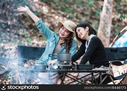 Young pretty taking photo by camera two female friends while sitting at the camping tent in forest on holiday vacation, Young Asian group woman travel outdoor camping.
