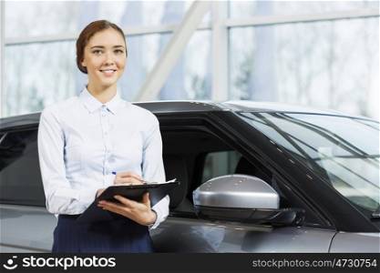 Young pretty woman dealer in showroom standing near car . I will help you to choose car