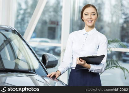 Young pretty woman dealer in showroom standing near car . I will help you to choose car