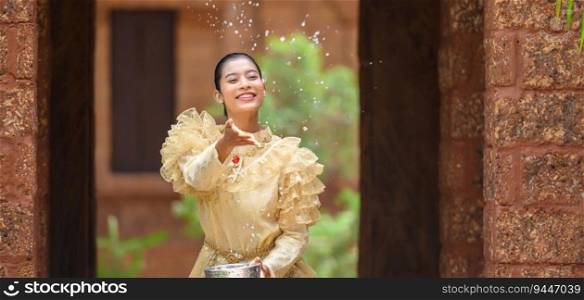 Young pretty woman dress in beautiful Thai costumes splashing water in temples and preserve the good culture of Thai people during Songkran festival. Thai New Year, Family Day in April