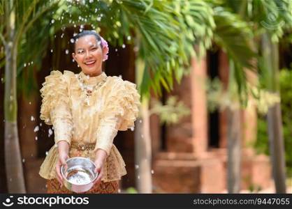 Young pretty woman dress in beautiful Thai costumes splashing water in temples and preserve the good culture of Thai people during Songkran festival. Thai New Year, Family Day in April