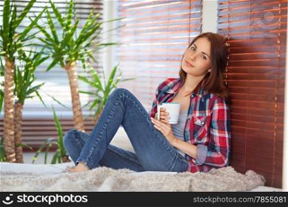 Young pretty woman drinking coffee / tea on sofa at home