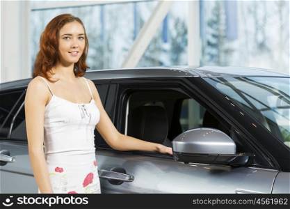 Young pretty woman in car salon standing near car. My new car