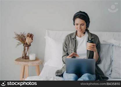 Young pretty woman in headset has online meeting at home. European girl in casual wear has coffee and internet conference. Homey girl having video call. Leisure and communication on quarantine.. Young pretty woman in headset has online meeting at home. Leisure and communication on quarantine.