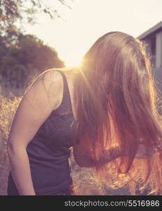 Young Pretty Woman In The Autumn Park at Sunset. Backlit. Her face hidden by long blond hair. Bended pose.