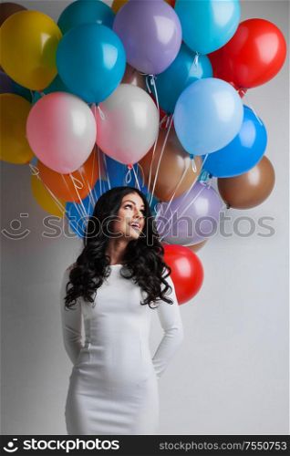 Young pretty woman in white dress with colored balloons on white background with copy space for text. Woman with colored balloons