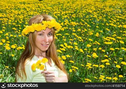 Young pretty woman in wreath of dandelions in the meadow solar day