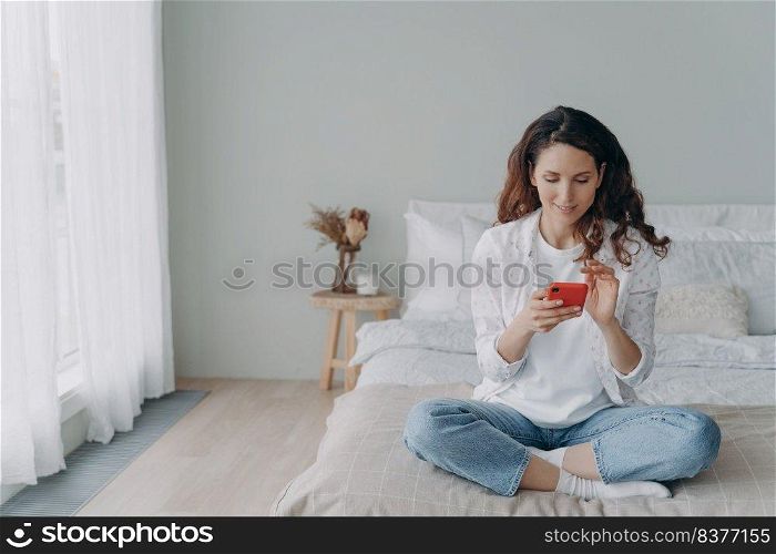 Young pretty woman is chatting on phone at home. Happy european girl in casual wear is texting and receiving messages. Leisure and communication concept. Homey girl having good time.. Young pretty woman is chatting on phone at home. Happy european girl in casual wear is texting.