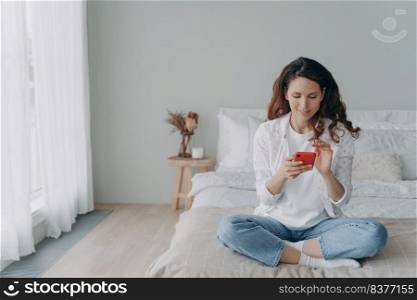 Young pretty woman is chatting on phone at home. Happy european girl in casual wear is texting and receiving messages. Leisure and communication concept. Homey girl having good time.. Young pretty woman is chatting on phone at home. Happy european girl in casual wear is texting.