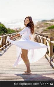 Young pretty woman moving a beautiful white dress in Spanish fashion on a boardwalk on the beach.. Young woman wearing a beautiful white dress in Spanish fashion on a boardwalk on the beach.