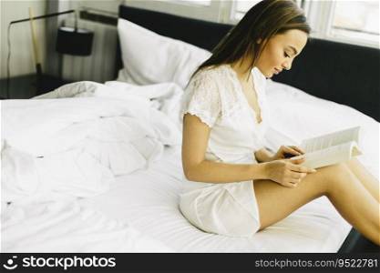 Young pretty woman sitting on a bed and reading a book
