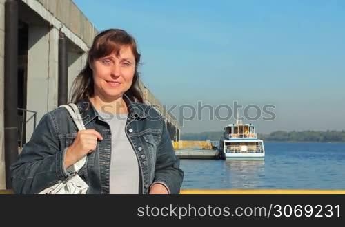 young pretty woman stands near shore and smiles, boat on background