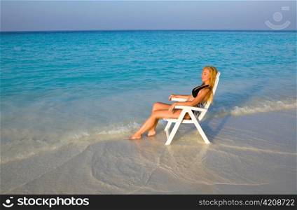 Young pretty woman tans in beach chair, it put in ocean