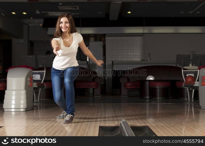 Young pretty woman throwing a bowling ball. At bowling club