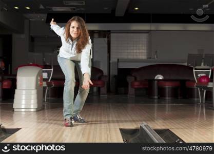 Young pretty woman throwing a bowling ball. At bowling club