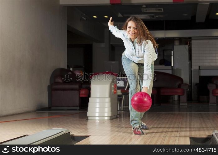 Young pretty woman throwing a bowling ball. At bowling club
