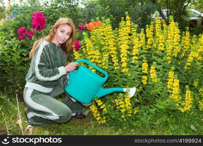 Young pretty woman waters flowers on garden