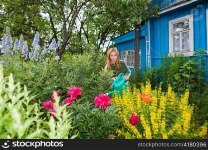 Young pretty woman waters flowers on garden-plot, focus in central part