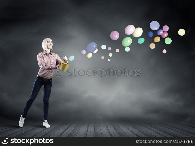 Young pretty woman with yellow bucket in hands. Girl splashing balloons from bucket
