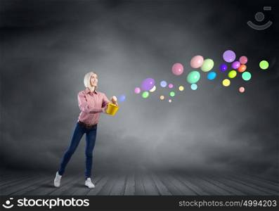 Young pretty woman with yellow bucket in hands. Girl splashing balloons from bucket