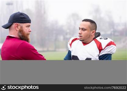young professional american football player discussing strategy together with coach during training match on the stadium field