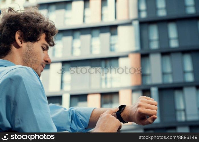Young progressive businessman using touchscreen smartwatch to check time, browsing internet in city area. Concept of electric hand gadget feature with mobile app, physical heart rate and time.. Young progressive businessman using touchscreen smartwatch to check time.