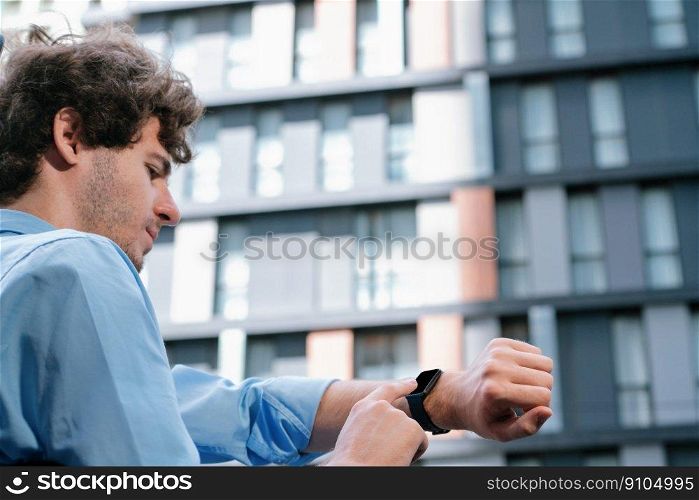 Young progressive businessman using touchscreen smartwatch to check time, browsing internet in city area. Concept of electric hand gadget feature with mobile app, physical heart rate and time.. Young progressive businessman using touchscreen smartwatch to check time.
