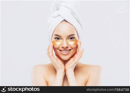 Young pure beautiful gentle woman with a towel on head standing naked isolated looking camera take care of her skin with under eye patches.