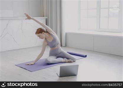 Young red haired european woman practicing yoga on exercise mat. Sportswoman is doing workout on floor. Female sports. E-learning and home online classes. Stay home on quarantine concept.. Young woman practicing yoga on exercise mat. Female sports and home online classes on quarantine.