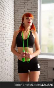 young red-haired girl in sportswear with a rope on a background of gray brick wall. girl with a rope