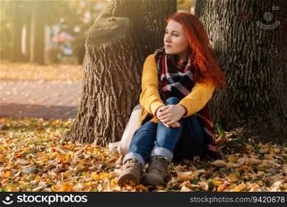 Young red-haired woman in yellow sweatshirt walks in autumn park. Lady is enjoying the sun in nature.. Young red-haired woman in yellow sweatshirt walks in autumn park. Lady is enjoying sun in nature.