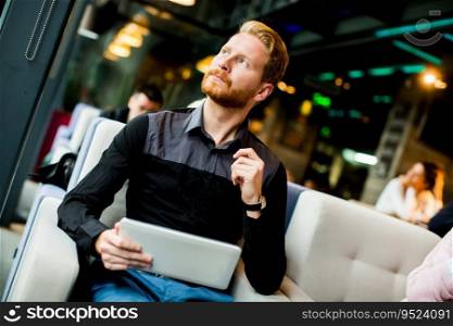 Young redhair man sitting in cafe and holding tablet