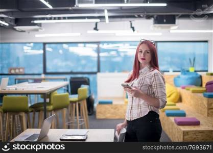 young redhead businesswoman reading a text message on her mobile phone while having a break in the modern startup office