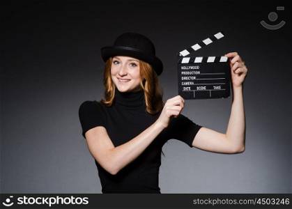 Young redhead girl in hat with movie board against grey background