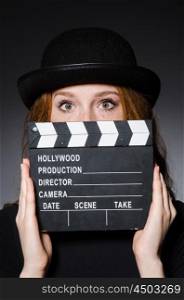 Young redhead girl in hat with movie board against grey background