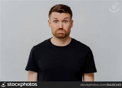 Young redhead man looking displeased, seeing something disgusting, dissatisfied guy in black tshirt looking at camera with pouted lips while standing over gray background. Negative feelings concept. Young dissatisfied guy with dissatisfied face expression