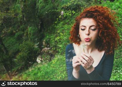young redhead woman blowing a dandelion